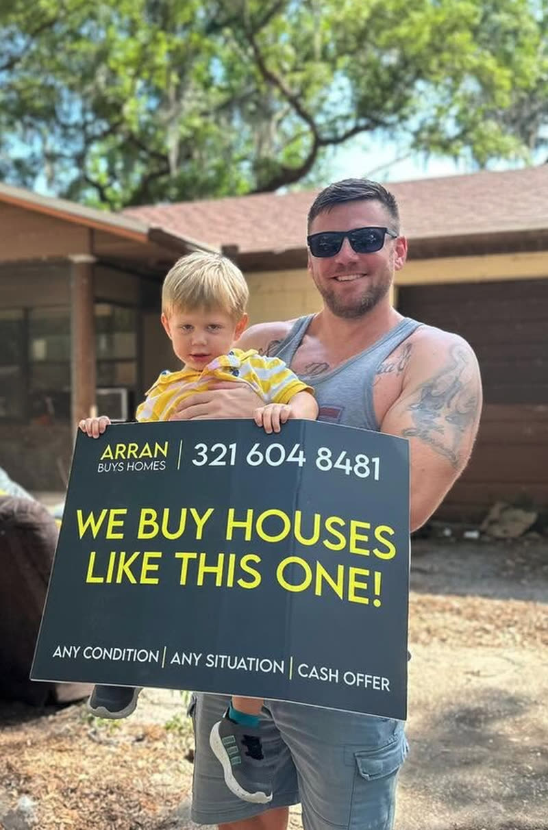Arran of Arran Buys Homes holding his son in front of a house he purchased in Central Florida